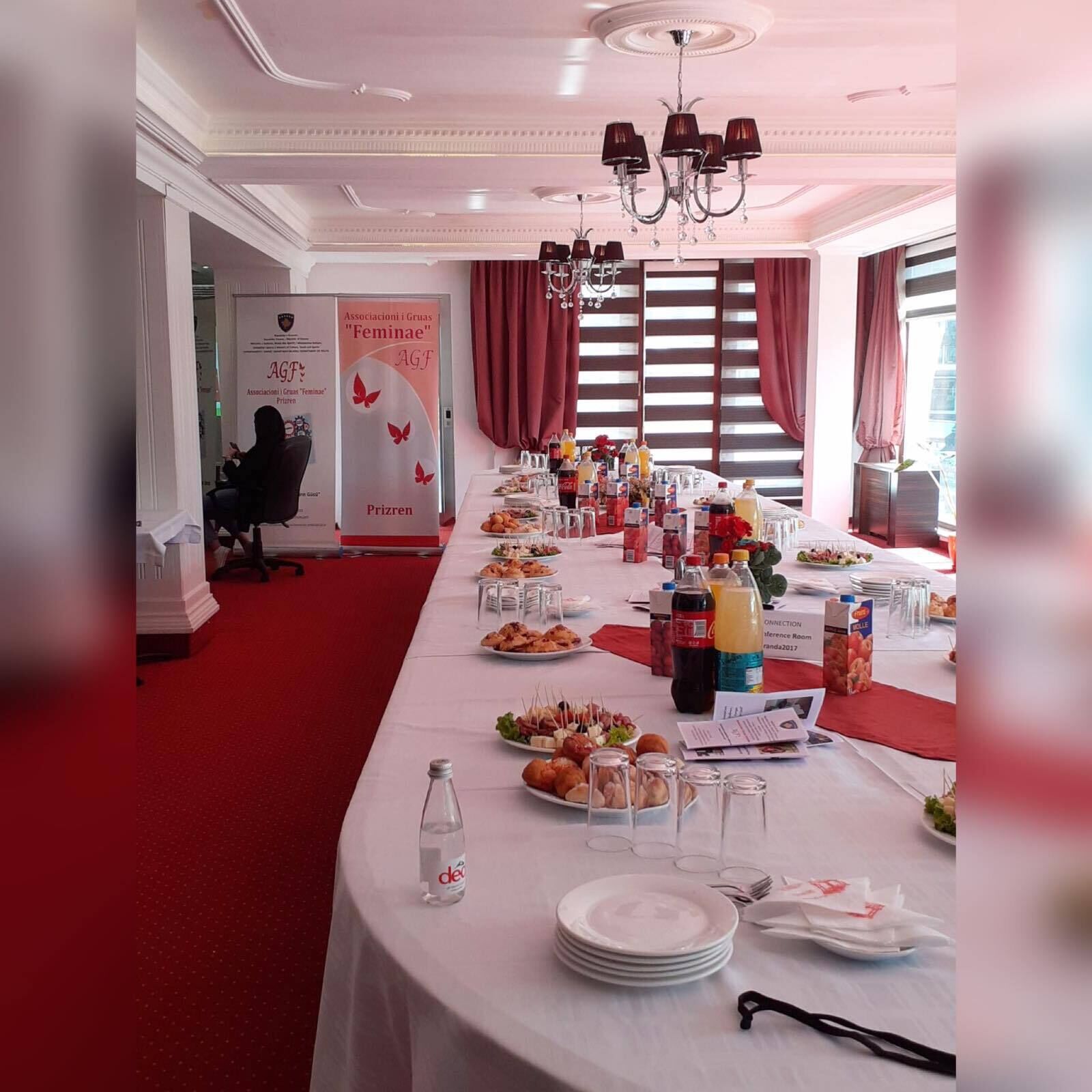 A conference room with a long table set for a meeting, featuring a banner for 'Associazioni i Gruas "Femminine" AGF' and a red carpet.