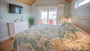 Ein Schlafzimmer mit Bett, Fernseher, Kommode, Fenster und Balkon.