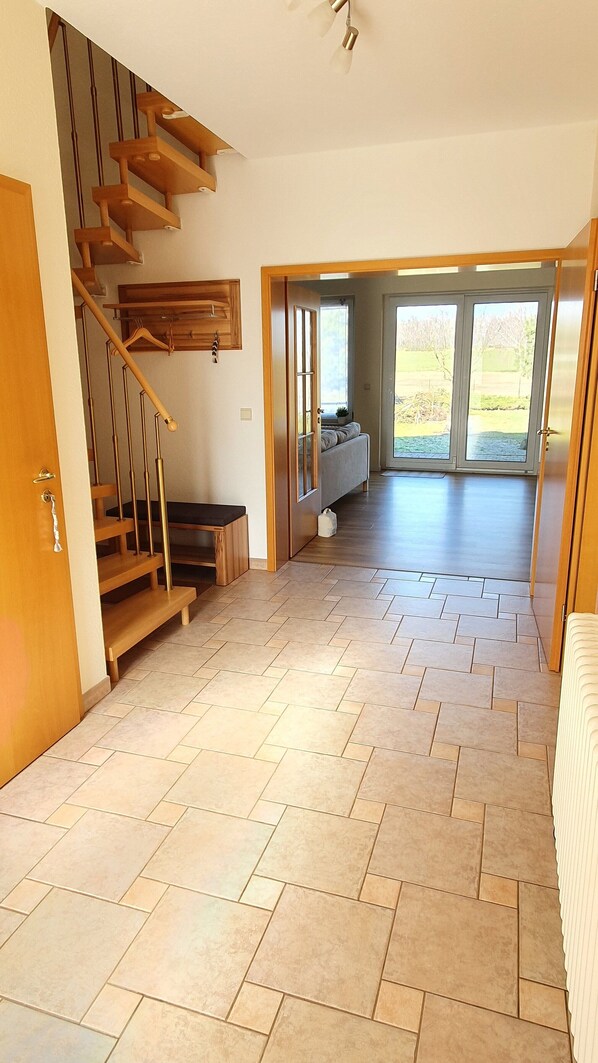 A spacious room with a herringbone-patterned floor, a wooden staircase, and a view through large glass doors to an outdoor area. - Large rural vacation home in a quiet location near the Spreewald (Dahme/Mark)