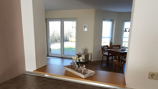 A kitchen with a dark countertop, light-colored cabinets, and a view into the dining area through an archway. - Large rural vacation home in a quiet location near the Spreewald (Dahme/Mark)