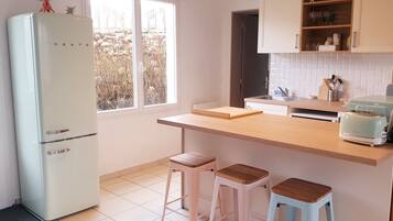 A compact kitchen with a white refrigerator, wooden countertop, two stools, and a toaster.
