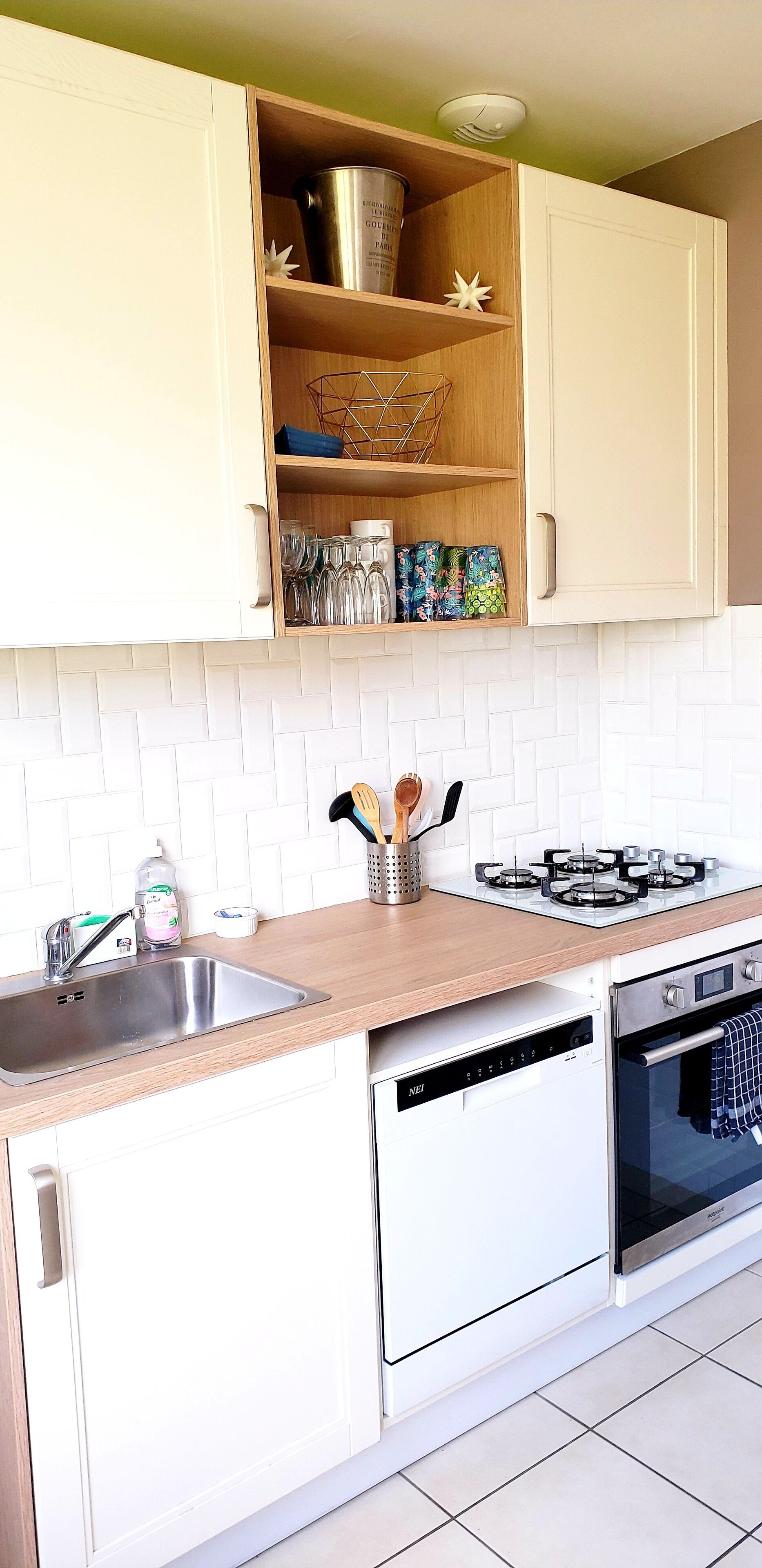 Een moderne keuken met witte kasten, een roestvrijstalen spoelbak, een vaatwasser, een fornuis en een betegelde achterwand.