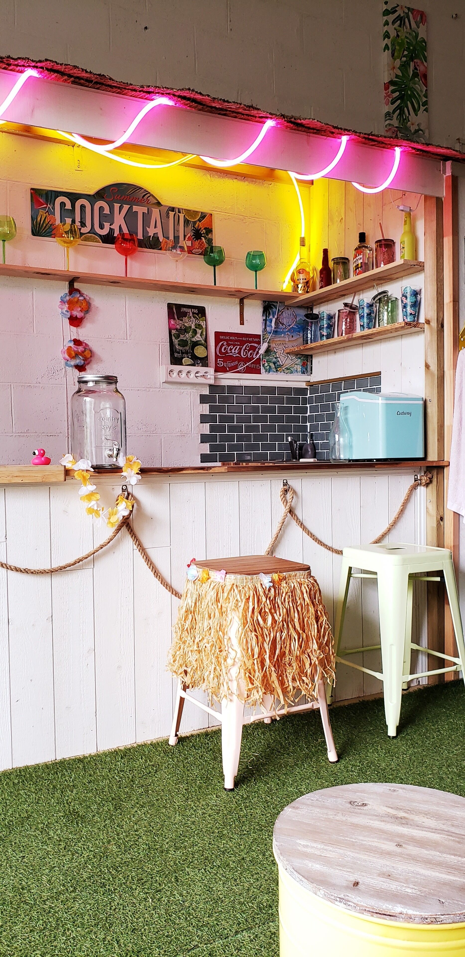 En tiki-bar med en neonreklamskylt, hyllor fulla med burkar, en Coca-Cola-skylt och en kylbox med Coors Light.