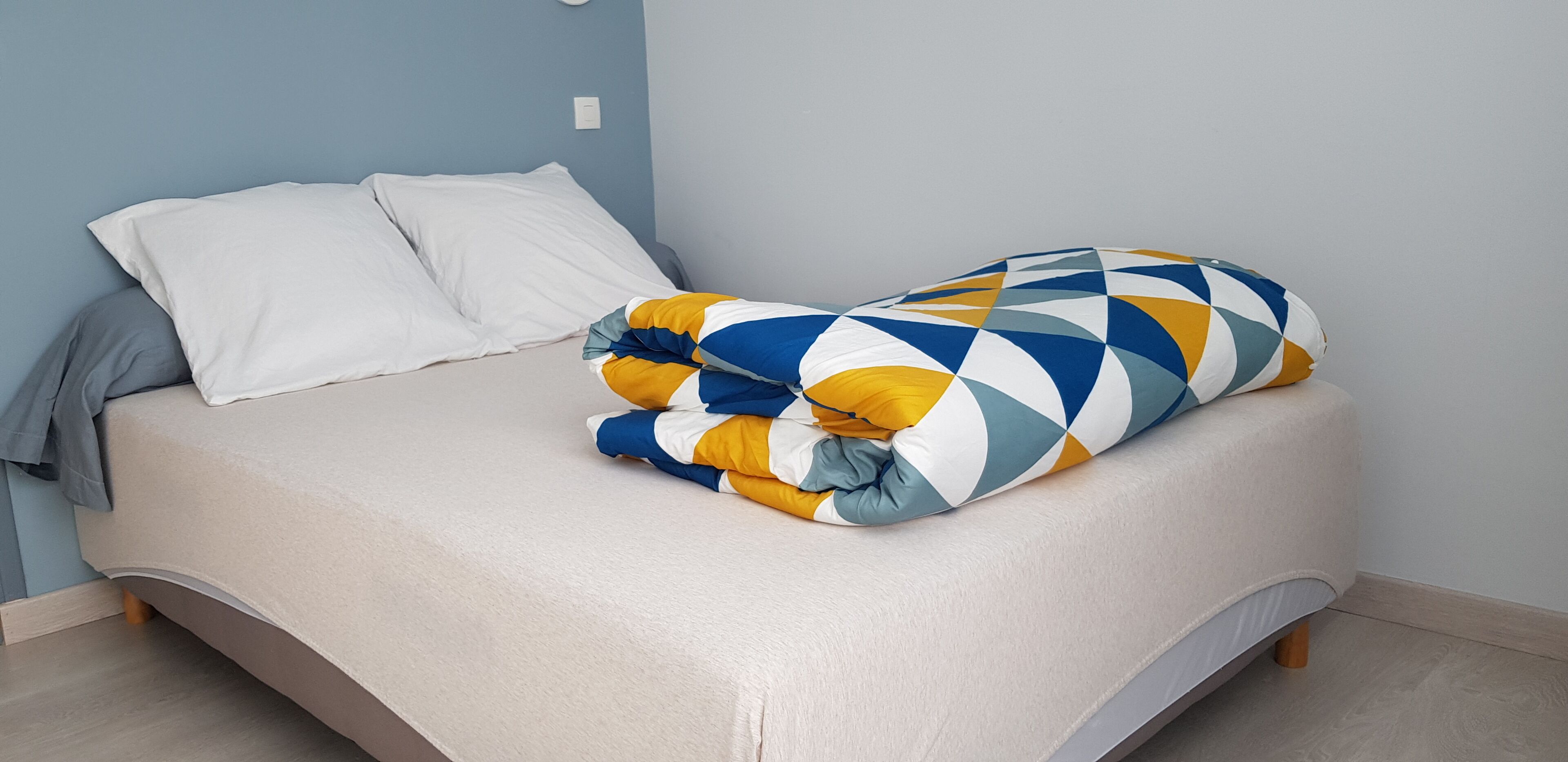A bed with a beige mattress, white pillows, and a colorful blanket.