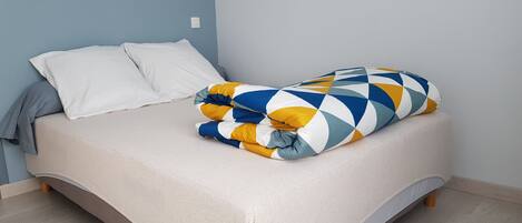 A bed with a beige mattress, white pillows, and a colorful blanket.