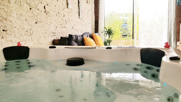 A spa room with a hot tub, a rustic wall, and a view of greenery outside. - Unlimited private indoor Jacuzzi at Mont saint-michel (Pontorson)