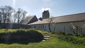 A traditional stone building with a steeply pitched roof, a small tower, and a well-maintained garden with a pathway leading to the entrance. - Unlimited private indoor Jacuzzi at Mont saint-michel (Pontorson)