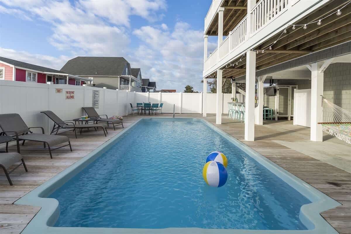 A swimming pool with lounge chairs and a covered area with tables and chairs.