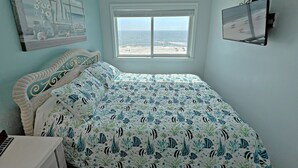 Un dormitorio con cama, ventana con vista a la playa y un cuadro en la pared.