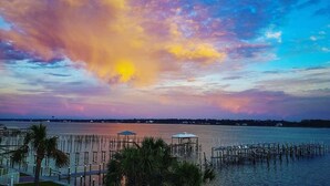 Vista al frente del agua con atardecer, palmeras y un muelle con quiosco.