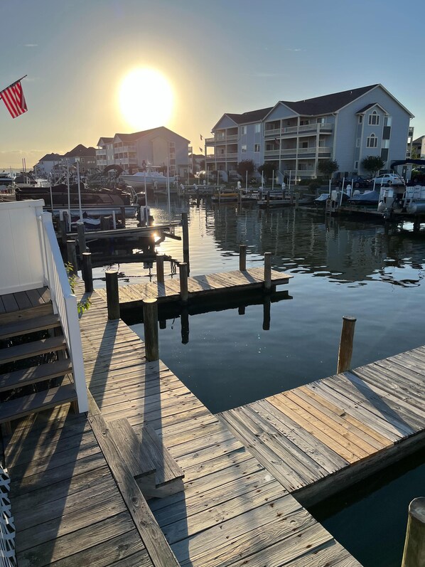 A marina with wooden docks and a clear view of the sun setting behind buildings.