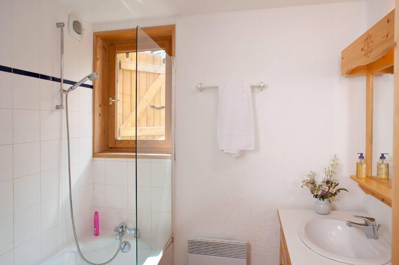A bathroom with a glass-enclosed shower, a wooden window, a white towel, a sink, and a mirror.