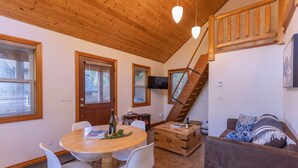 Een gezellige woonkamer met een houten trap, een eethoek met een ronde tafel en stoelen, en een comfortabele bank.