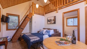 Een gezellige kamer met een bed, een houten tafel met een fles en glazen, een televisie en een trap.