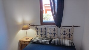 Et soveværelse med seng, natbord, lampe, gardiner og et vindue.