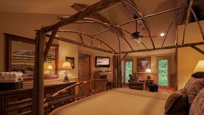 Une chambre spacieuse avec un grand lit, une tête de lit en bois, une télévision, un bureau avec une lampe et une fenêtre donnant sur un paysage verdoyant.