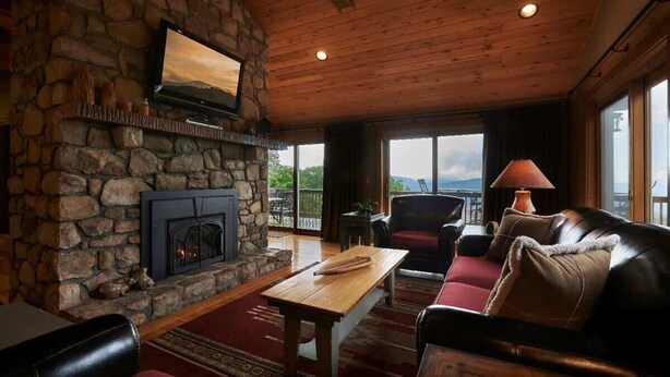 Un salon chaleureux avec une cheminée en pierre, un plafond en bois et une grande fenêtre offrant une vue panoramique.