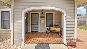 A house with a porch, a bench, and a small red wagon with flowers. - Deannies Cottage 2 Bedroom Cottage by RedAwning (Fredericksburg)
