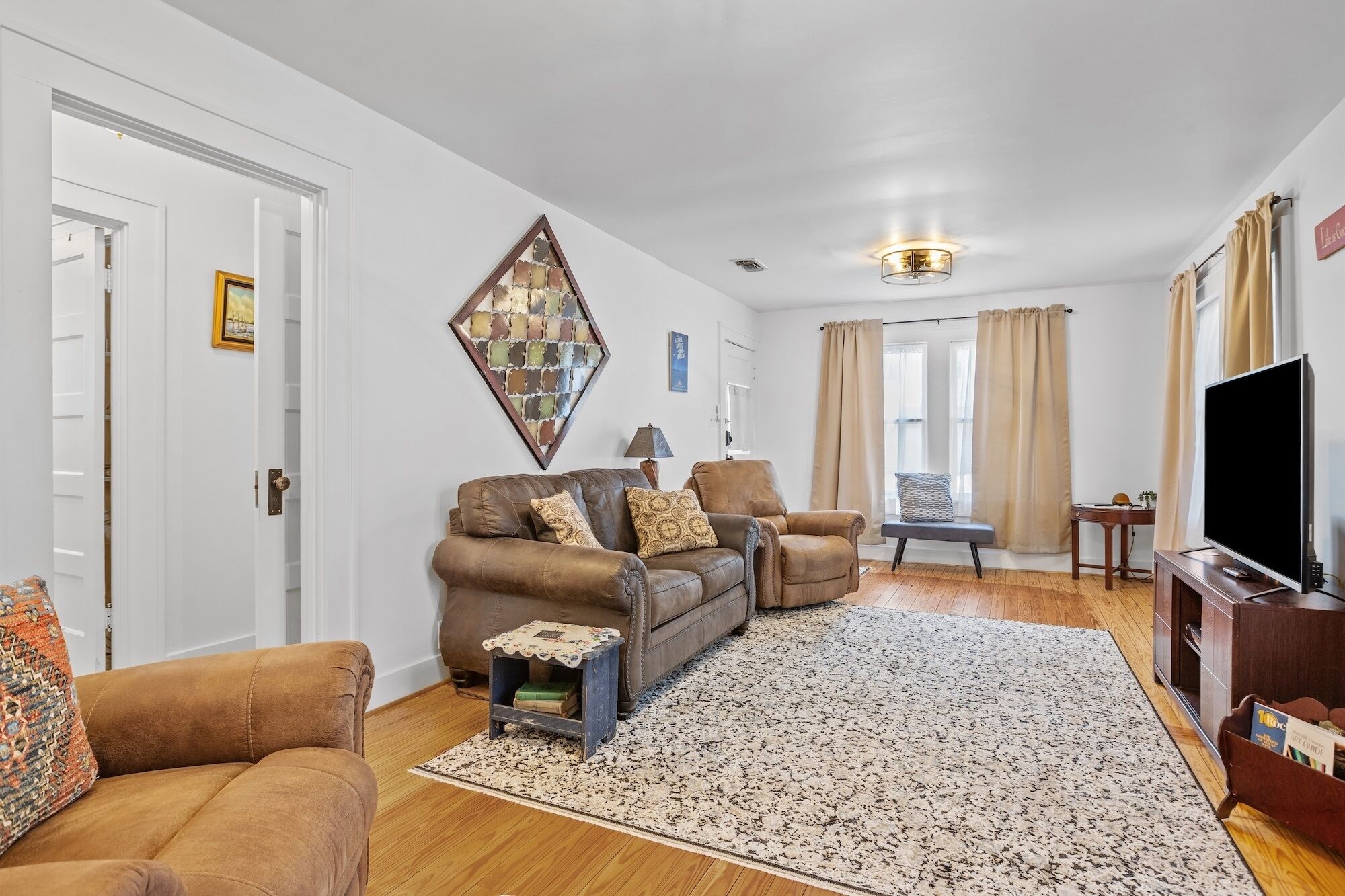 A living room with a brown leather sofa, a small side table, a television, and a patterned rug.