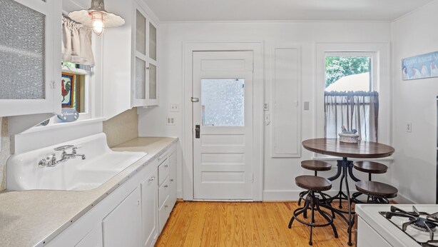 A kitchen with white cabinets, a sink, a stove, and a dining area with stools. - Deannies Cottage 2 Bedroom Cottage by RedAwning (Fredericksburg)