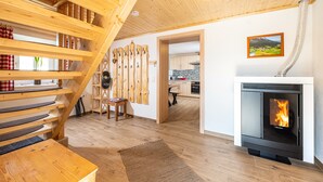 A wooden staircase leading to a loft, a fireplace with a visible fire, and a kitchen in the background. - Quaint, rustic vacation home with hut flair on the sunny side of the Grimming (Mitterberg-St.Martin)