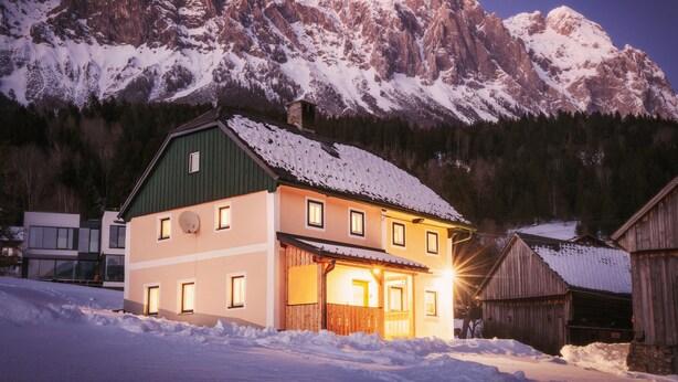 A two-story building with a green roof and multiple windows, surrounded by snow-covered mountains. - Quaint, rustic vacation home with hut flair on the sunny side of the Grimming (Mitterberg-St.Martin)