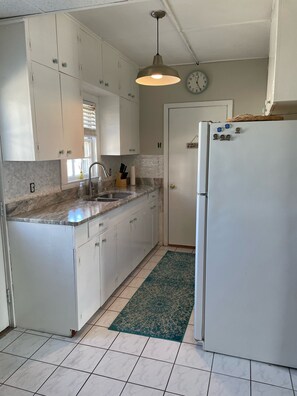 Kitchen features a stainless steel sink, refrigerator, and a clock mounted above.