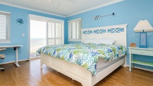 Quarto com cama, escrivaninha, cadeira, ventoinha no teto e janela com persianas.