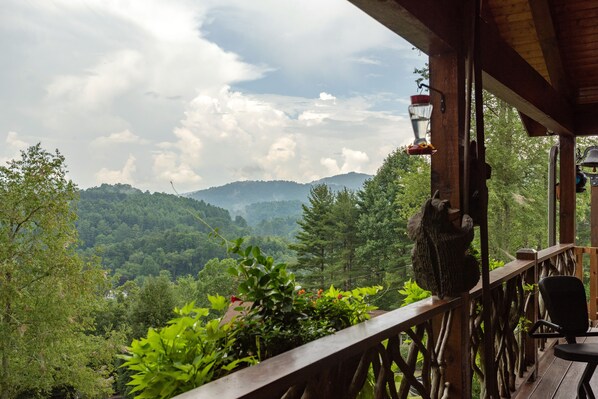 A wooden deck with a view of a forested valley and mountains.