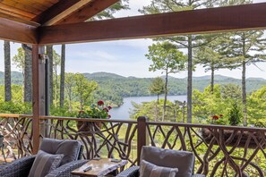 A wooden deck with wicker furniture overlooking a lake surrounded by trees.