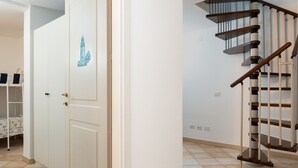 A room with a white door, a staircase with wooden handrails, and a tiled floor.