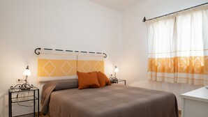 A neatly made bed with a headboard, two bedside tables with lamps, and a window with curtains.