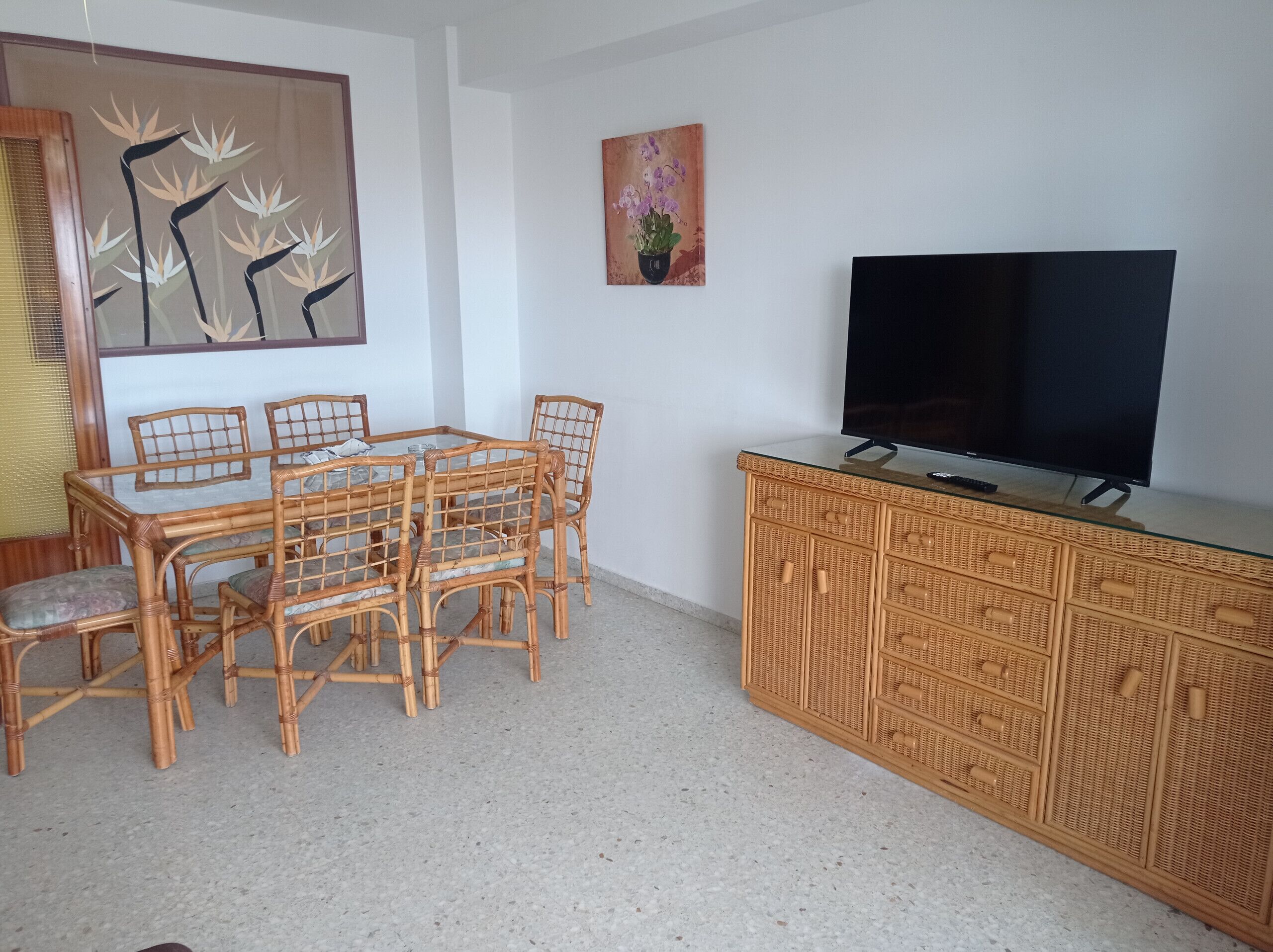 A dining area with a table and chairs, a television on a cabinet, and artwork on the wall.