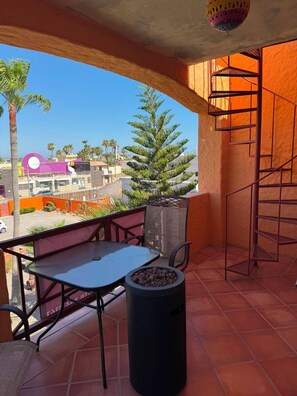 A balcony with a table and chairs, a trash bin, and a metal staircase.