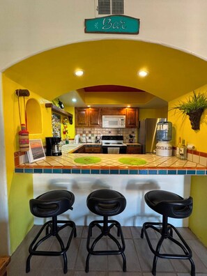 A kitchen with a bar area, three stools, and a sign that reads 'Bar'.