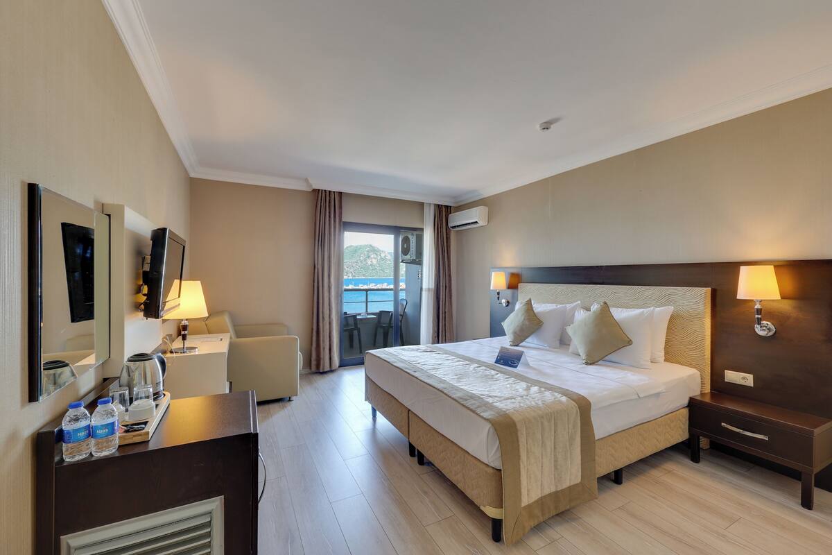 A hotel room with a large bed, bedside lamps, a desk with a chair, a desk lamp, a minibar, and a view of the outdoors.