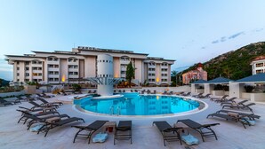 Un hotel con una piscina grande rodeada de tumbonas y un edificio con un llamativo letrero 'FANOS'.