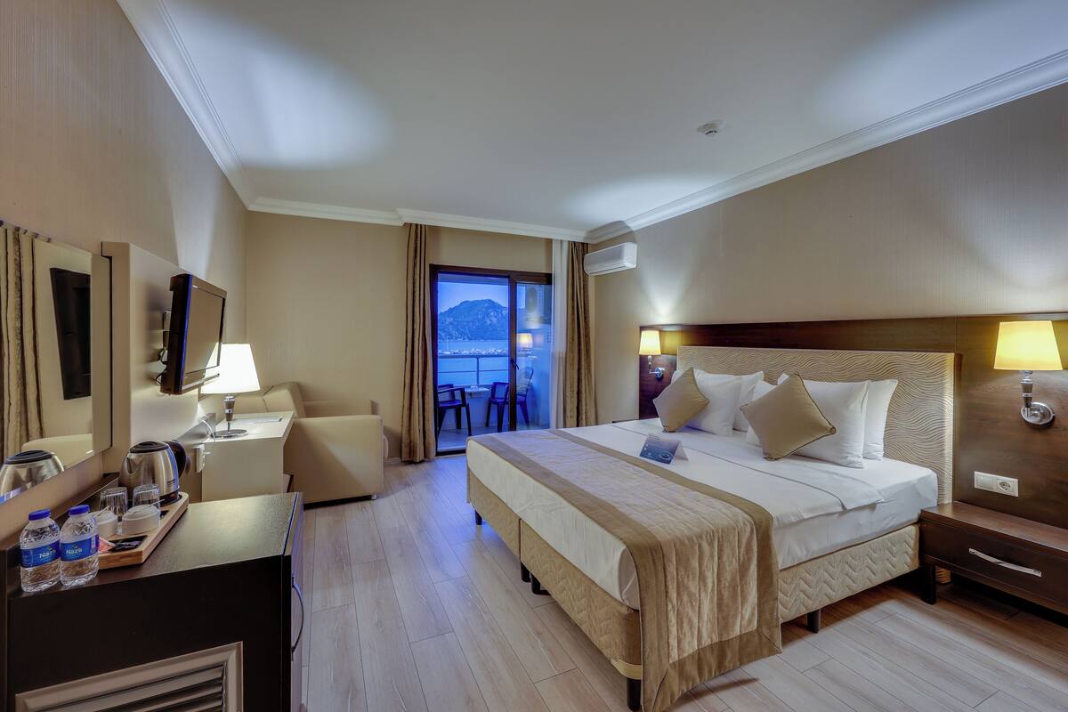 A hotel room with a bed, bedside table, lamp, and a view of the sea.