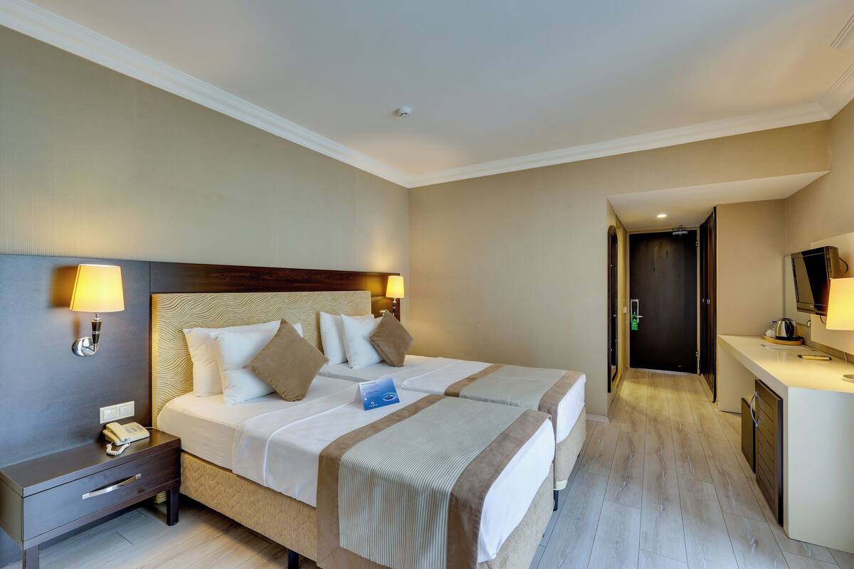 A hotel room with two beds, a nightstand, a desk, and a mirror.