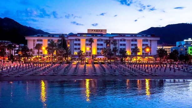Un hotel con una piscina grande, palmeras y montañas al fondo.