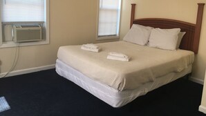 Cama bem arrumada com duas toalhas dobradas, cabeceira de madeira e janela com persianas.