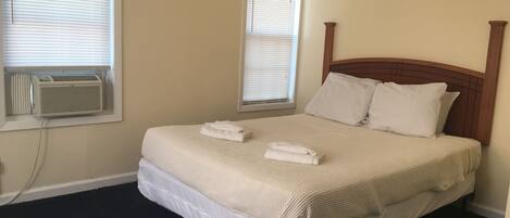A neatly made bed with two folded towels, a wooden headboard, and a window with blinds.