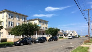 Rua residencial com casas de vários andares, carros estacionados e céu azul.