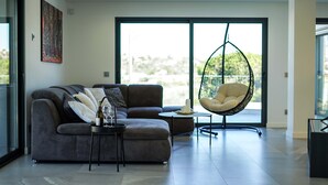 A modern living room with a grey sectional sofa, a hanging chair, and a small round table. - Villa Videira - By Dalma Portuguesa (Albufeira)
