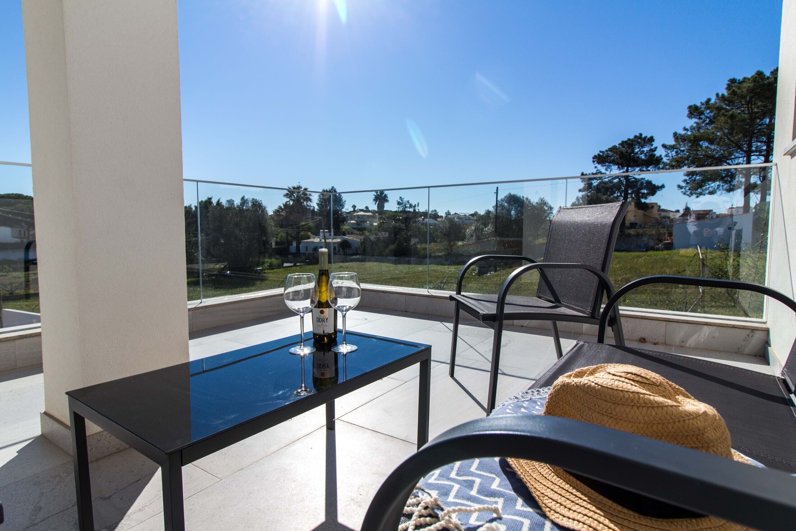 A balcony with a glass table, two wine glasses, and a woven hat.