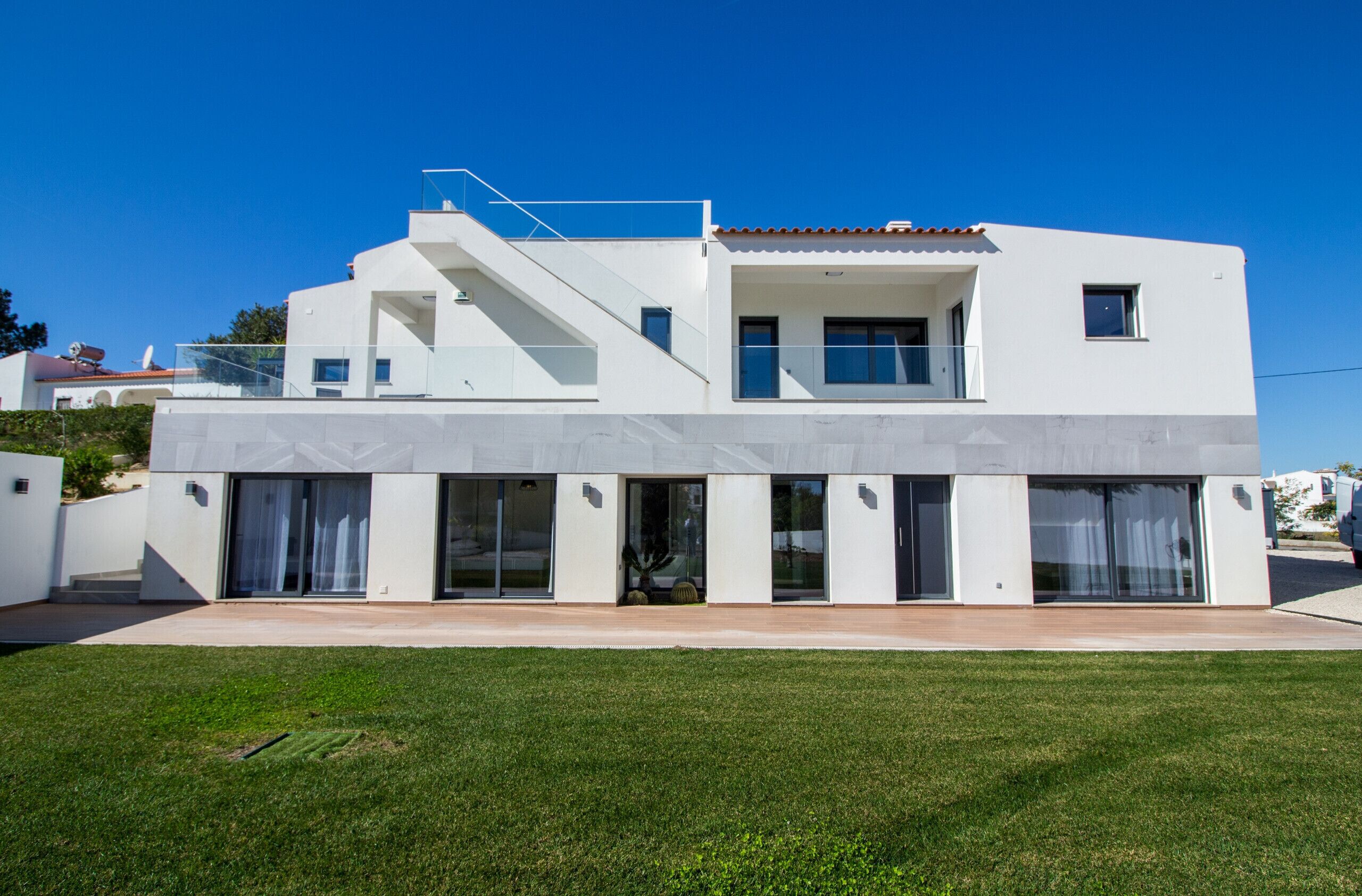 Uma casa moderna de dois andares com telhado plano, grandes janelas de vidro e uma escadaria visível que leva ao andar superior.