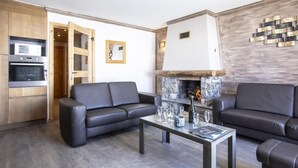 Un salon moderne avec deux canapés en cuir noir, une table basse en verre, une cheminée intégrée et un meuble en bois doté d’un four.