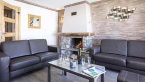 Un salon moderne avec deux canapés en cuir, une table basse en verre, une cheminée en pierre et un panneau mural en bois.