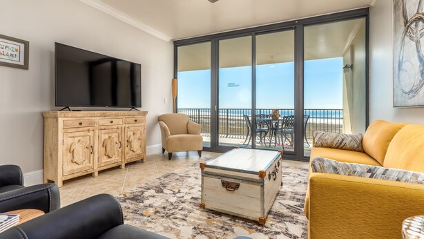 A living room with a television, wooden cabinet, sofa, and a view of the balcony. - Upscaled Gulf Front Condo, Stunning Views! - Ride The Wave (Dauphin Island)