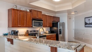 A modern kitchen with wooden cabinets, granite countertops, stainless steel appliances, and a welcome sign. - Upscaled Gulf Front Condo, Stunning Views! - Ride The Wave (Dauphin Island)